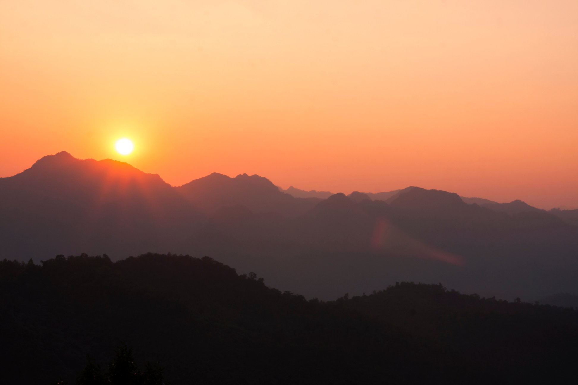 Sun shining through silhouetted mountains.